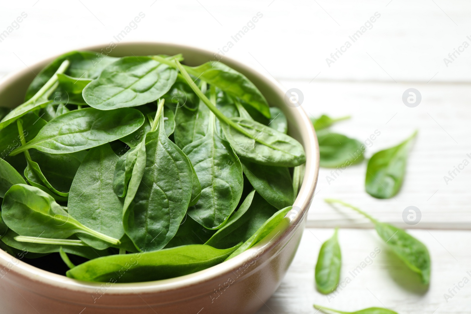 Photo of Bowl of fresh green healthy spinach on white wooden table, closeup