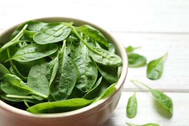 Photo of Bowl of fresh green healthy spinach on white wooden table, closeup