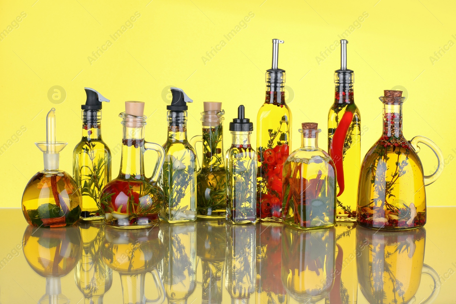 Photo of Cooking oil with different spices and herbs in bottles on yellow background