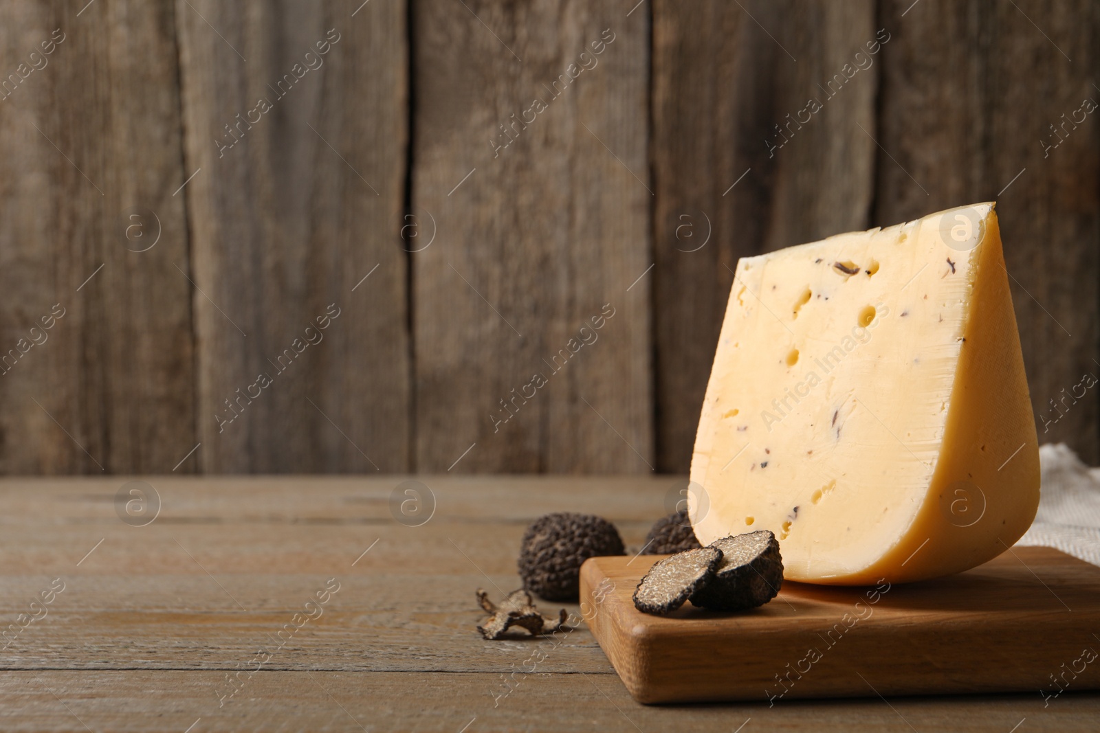 Photo of Delicious cheese and fresh black truffles on wooden table. Space for text