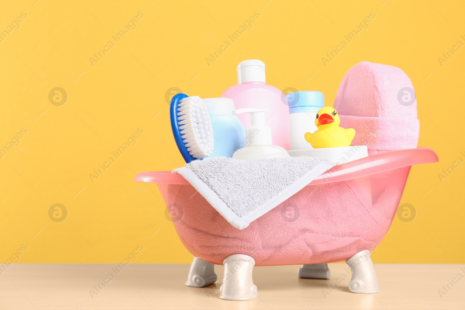 Photo of Baby cosmetic products, toy and towel on table against color background