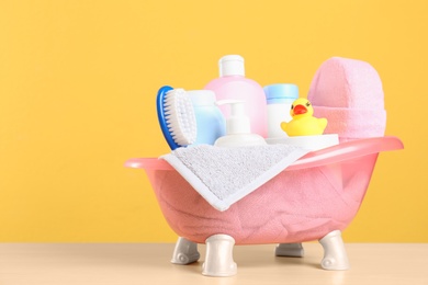 Photo of Baby cosmetic products, toy and towel on table against color background