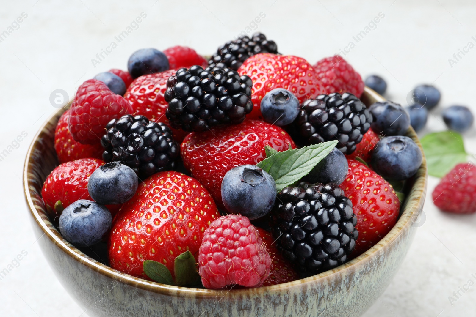 Photo of Different fresh ripe berries in bowl on table, closeup