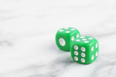 Photo of Two green game dices on white marble table, closeup