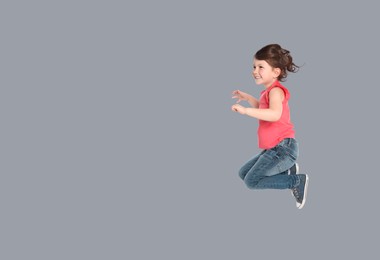Cute girl jumping on grey background, space for text