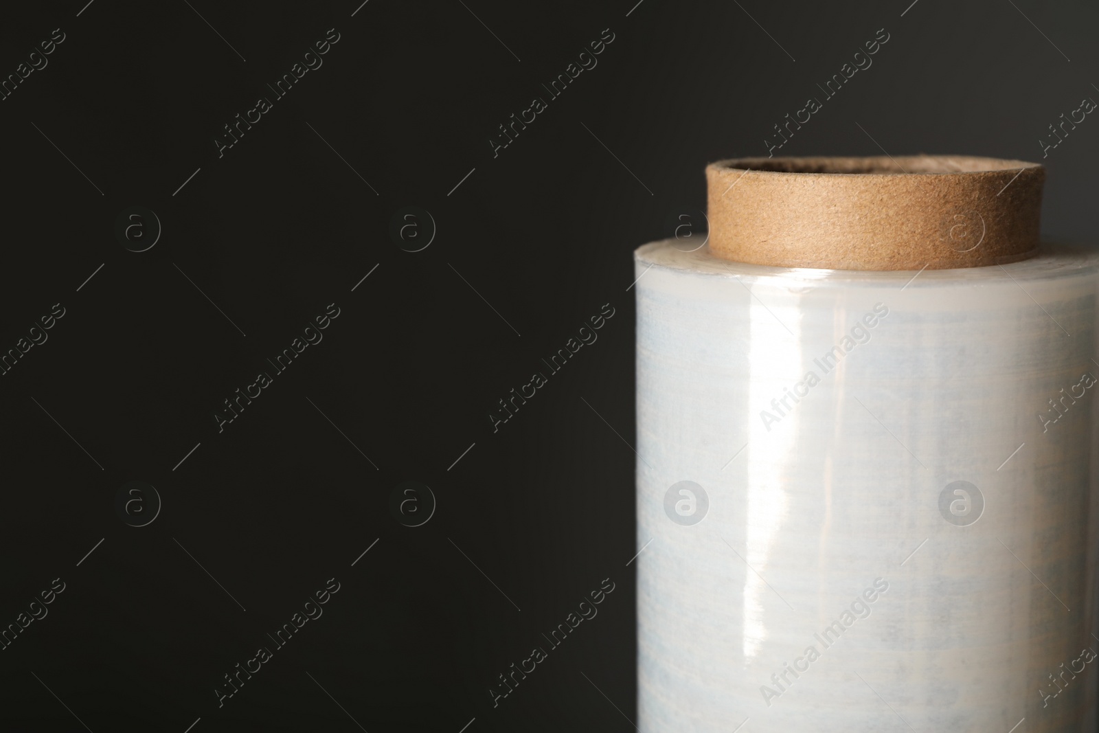 Photo of Roll of plastic stretch wrap film on black background, closeup. Space for text