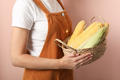 Woman with basket of corn cobs on coral background, closeup