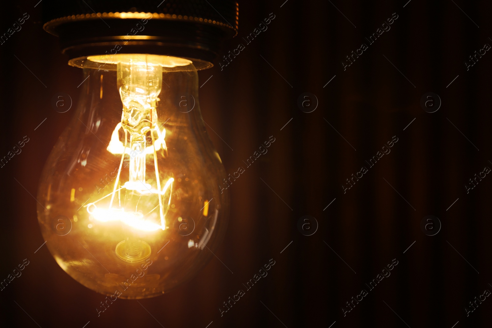 Photo of Hanging modern lamp bulb against dark background, closeup. Space for text