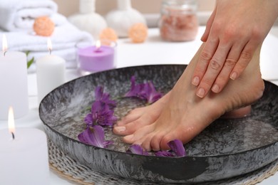 Photo of Woman soaking her feet in bowl with water and flowers on floor, closeup. Spa treatment