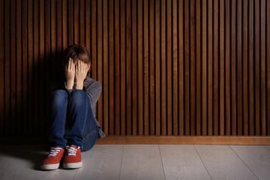 Photo of Little girl closing her eyes on floor indoors, space for text. Child in danger