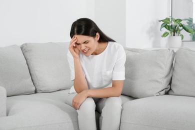 Photo of Young woman suffering from headache on sofa at home. Hormonal disorders