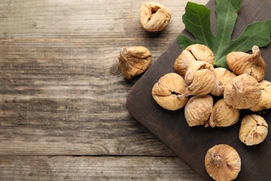 Board with tasty dried figs and green leaf on wooden table, flat lay. Space for text