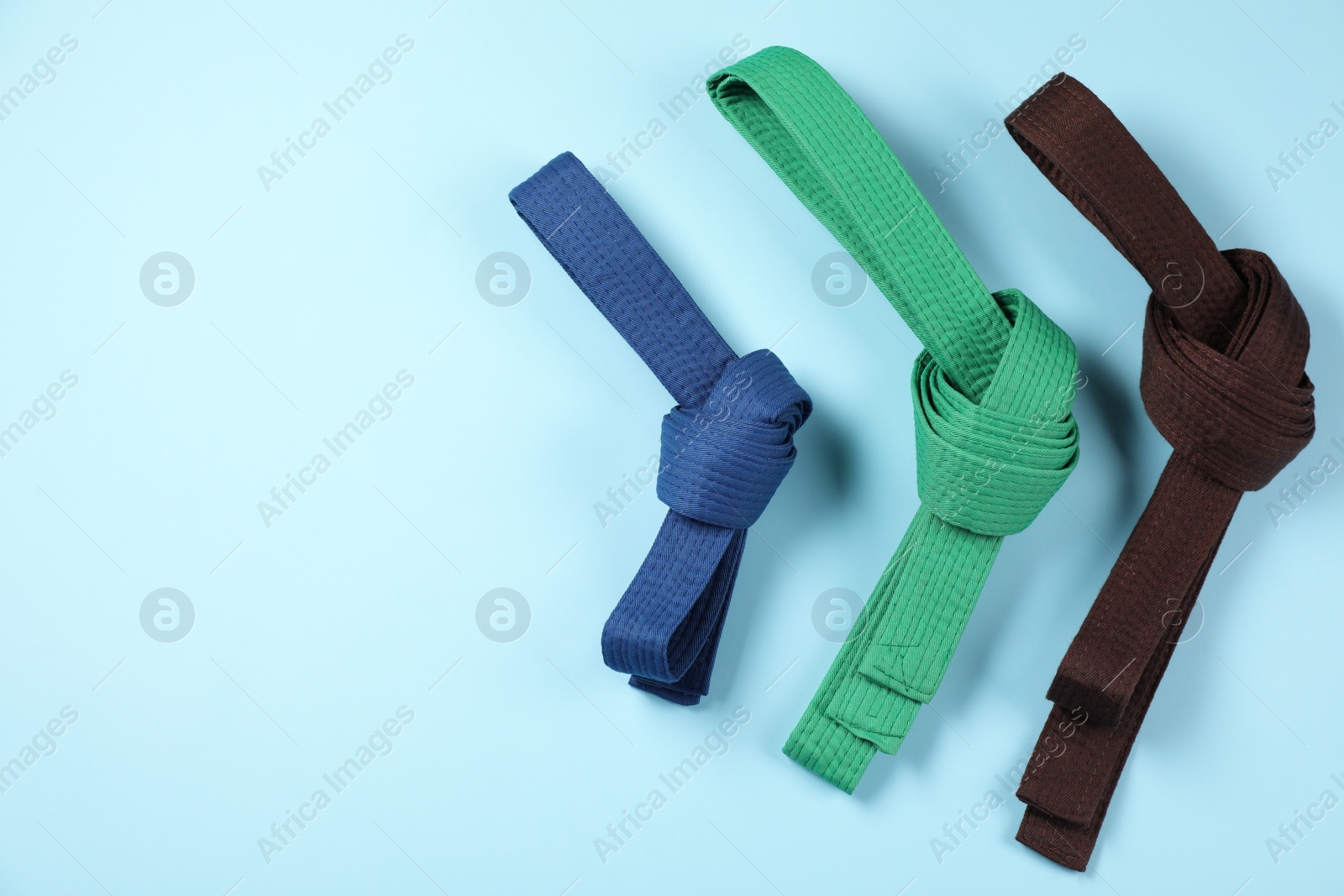 Photo of Colorful karate belts on light blue background, flat lay. Space for text