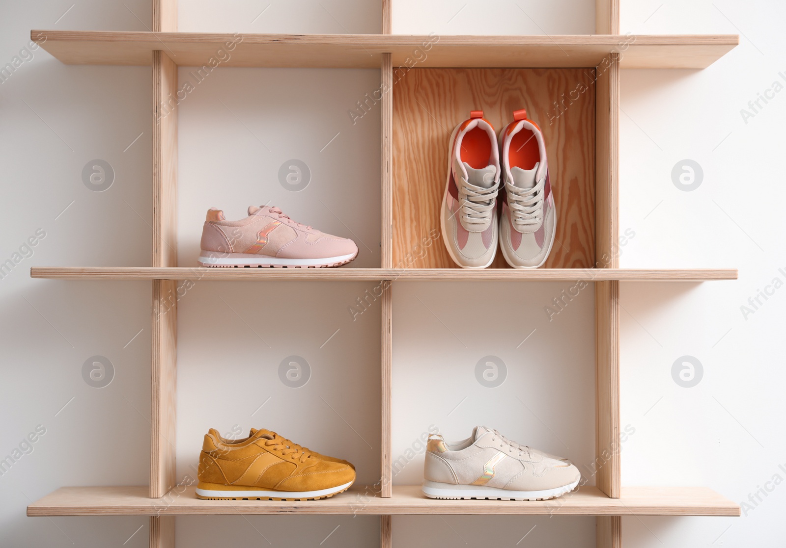 Photo of Wooden shelving unit with stylish women's sneakers on white wall