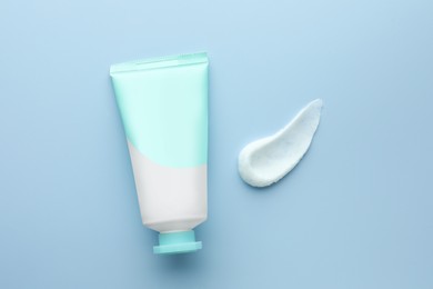 Photo of Sample of hand cream and tube on light blue background, top view