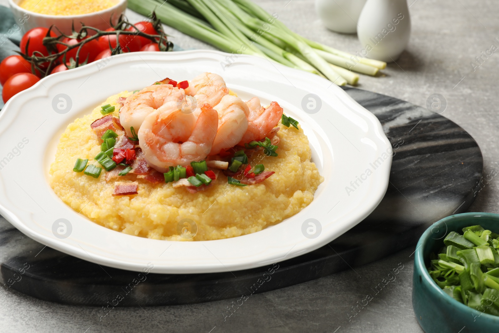 Photo of Plate with fresh tasty shrimps, bacon, grits, green onion and pepper on gray table, closeup