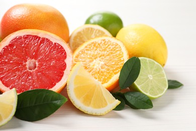 Photo of Different cut and whole citrus fruits on white wooden table, closeup