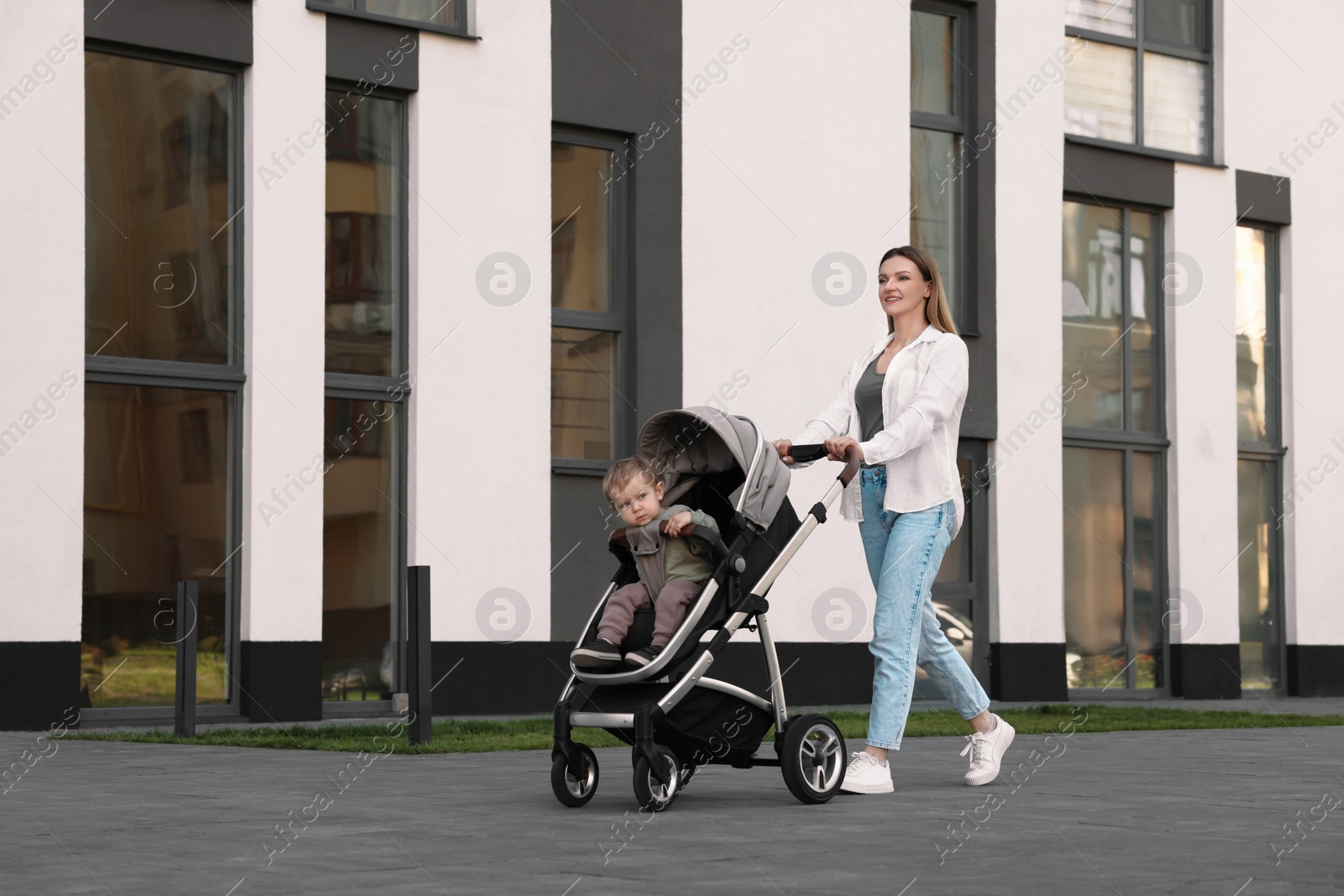 Photo of Happy nanny with cute little boy in stroller walking outdoors