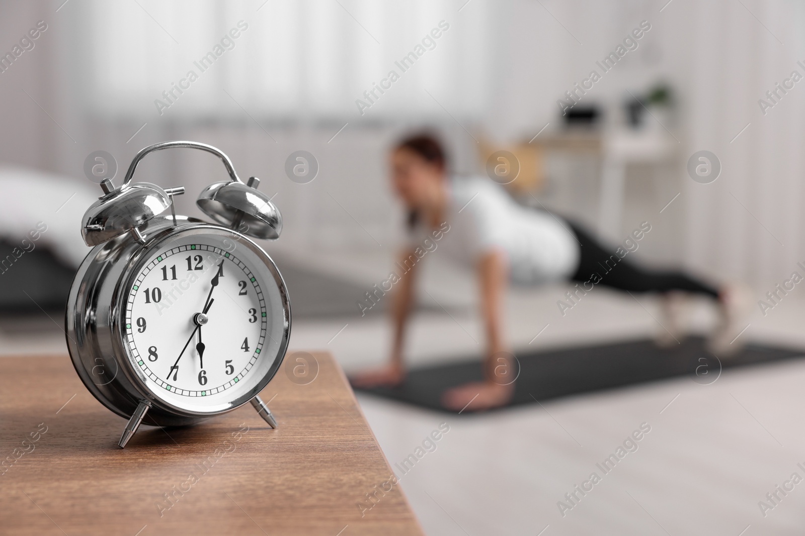 Photo of Morning routine. Alarm clock on wooden table and woman doing exercise, selective focus. Space for text