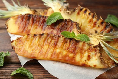 Photo of Tasty grilled pineapple pieces and mint leaves on wooden table, closeup