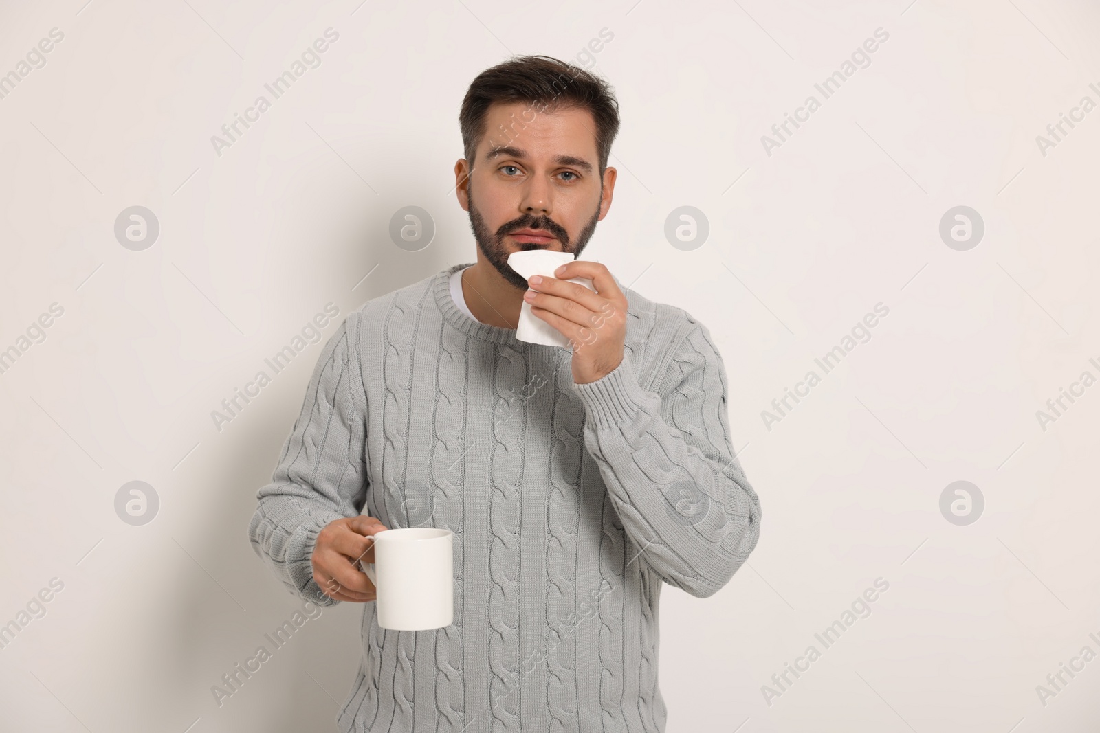 Photo of Sick man with tissue and cup of drink on light grey background. Cold symptoms