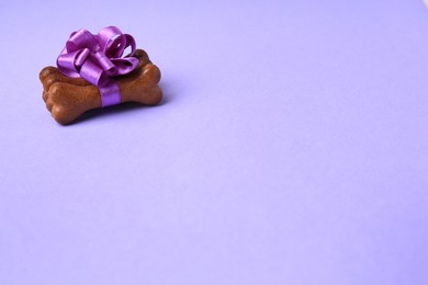 Photo of Bone shaped dog cookies with beautiful bow on purple background, space for text