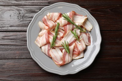 Slices of raw bacon and rosemary on dark wooden table, top view