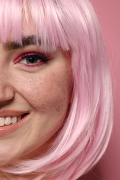 Smiling woman with bright makeup and fake freckles on pink background, closeup