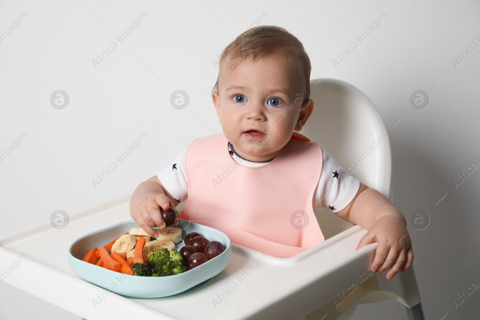 Photo of Cute little baby wearing bib while eating on white background