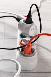 Power strip with different electrical plugs on white laminated floor, closeup