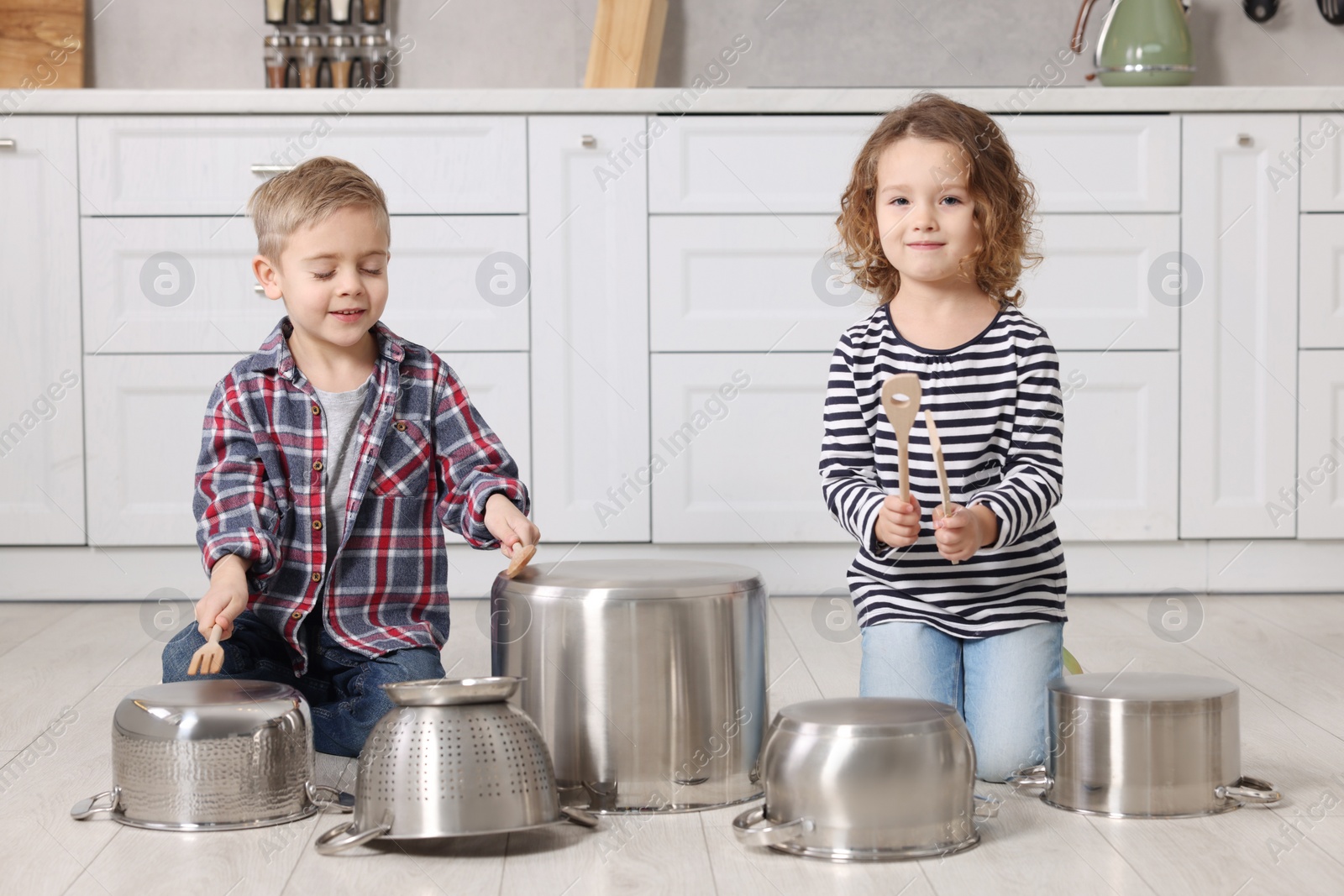 Photo of Little children pretending to play drums on pots in kitchen