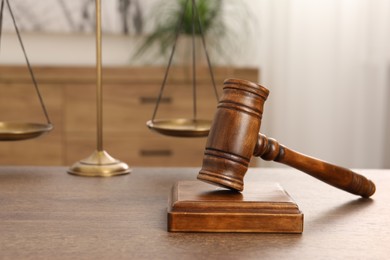 Photo of Wooden gavel, sound block and scales on table indoors, closeup. Space for text