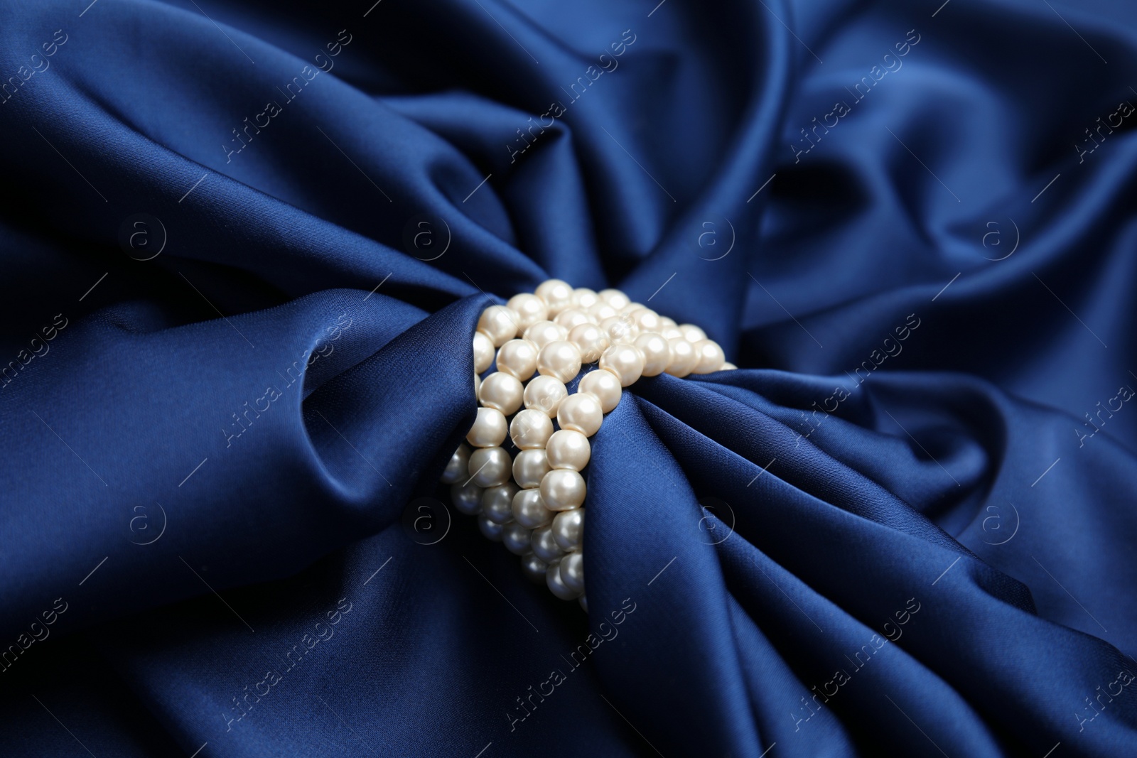 Photo of Beautiful pearls with dark blue silk as background, closeup