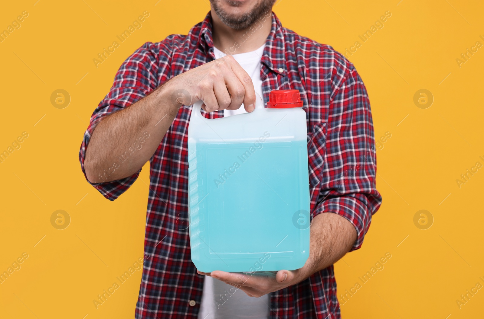 Photo of Man holding canister with blue liquid on orange background, closeup