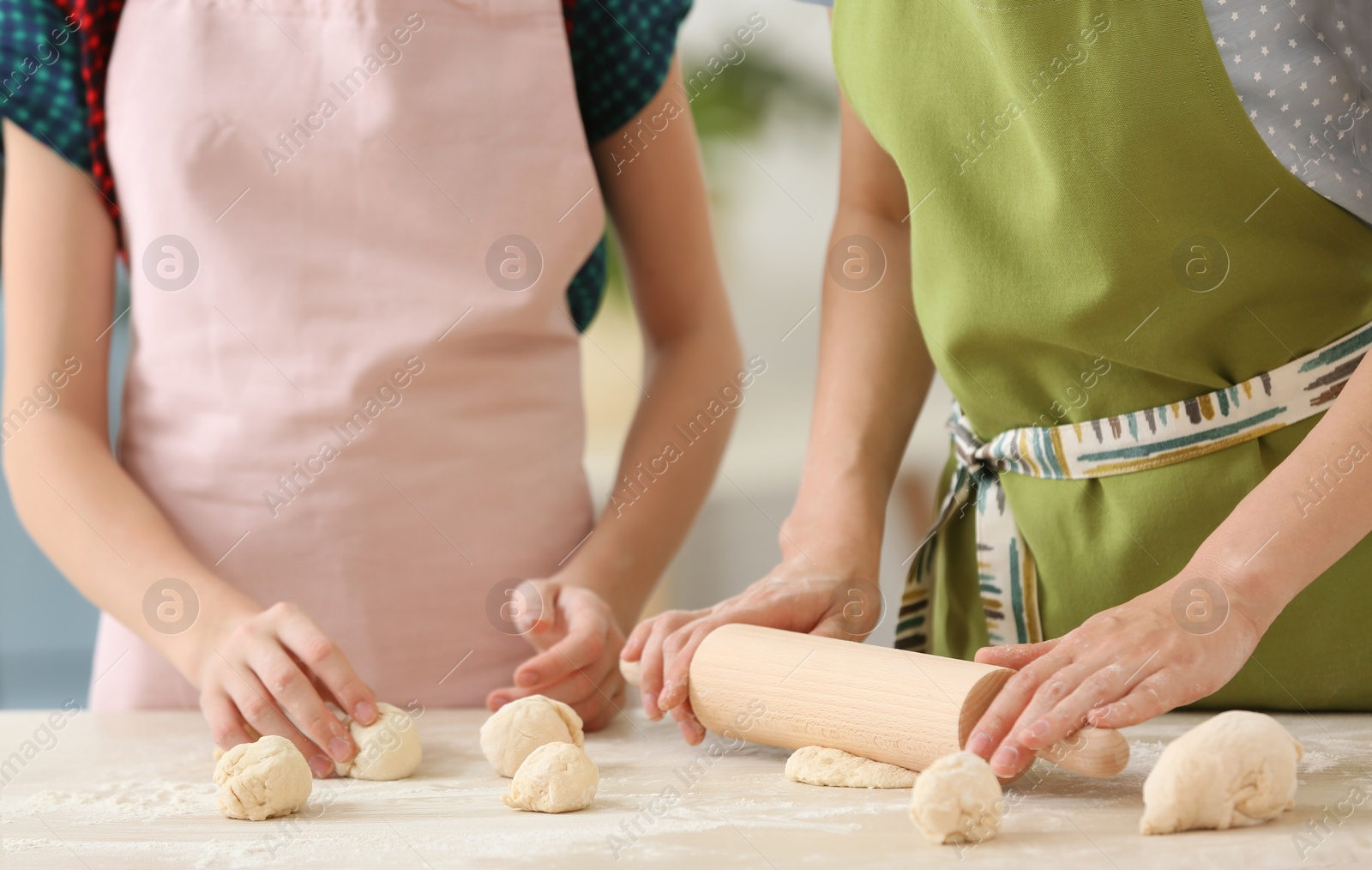 Photo of Mother and her daughter preparing dough at table, closeup