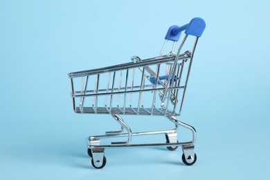 Small metal shopping cart on light blue background