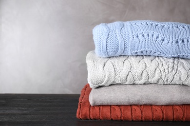 Image of Stack of folded warm sweaters on black wooden table. Space for text