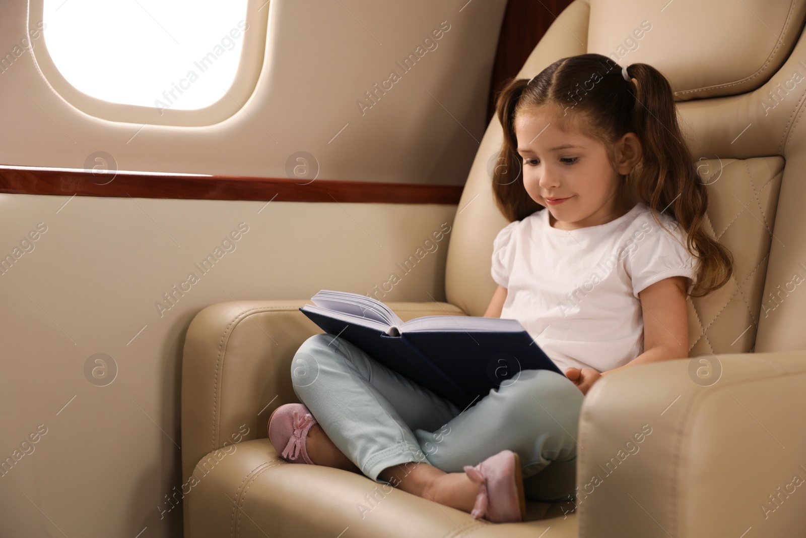 Photo of Cute little girl reading book in airplane during flight