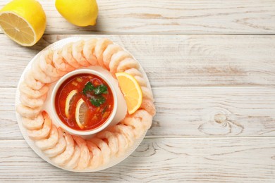 Tasty boiled shrimps with cocktail sauce and lemon on white wooden table, top view. Space for text