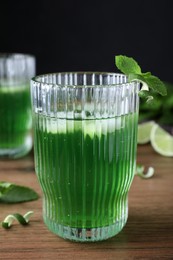 Photo of Delicious mint liqueur with green leaves and ice cubes on wooden table