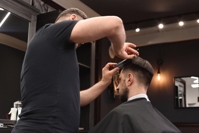 Professional hairdresser cutting man's hair in barbershop, low angle view