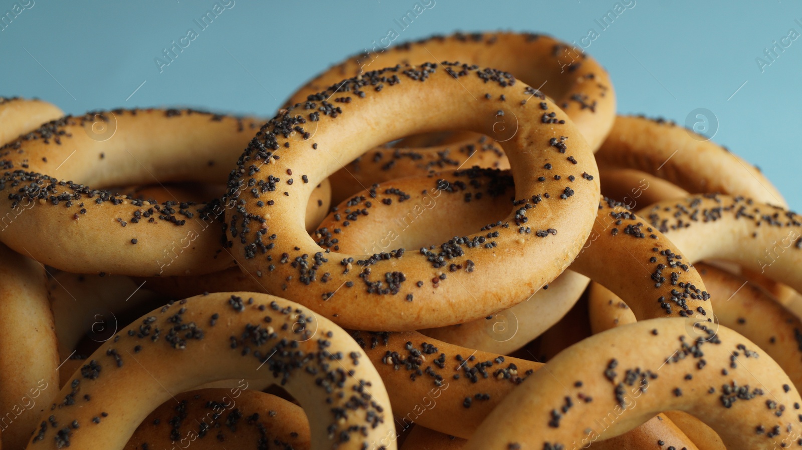 Photo of Many delicious ring shaped Sushki (dry bagels) on light blue background, closeup