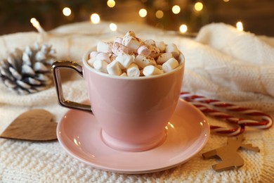 Photo of Cup of tasty cocoa with marshmallows, candy canes and Christmas decor on knitted plaid indoors