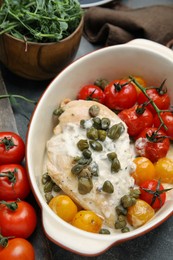 Photo of Delicious baked chicken fillet with capers, sauce and tomatoes in baking dish on grey table