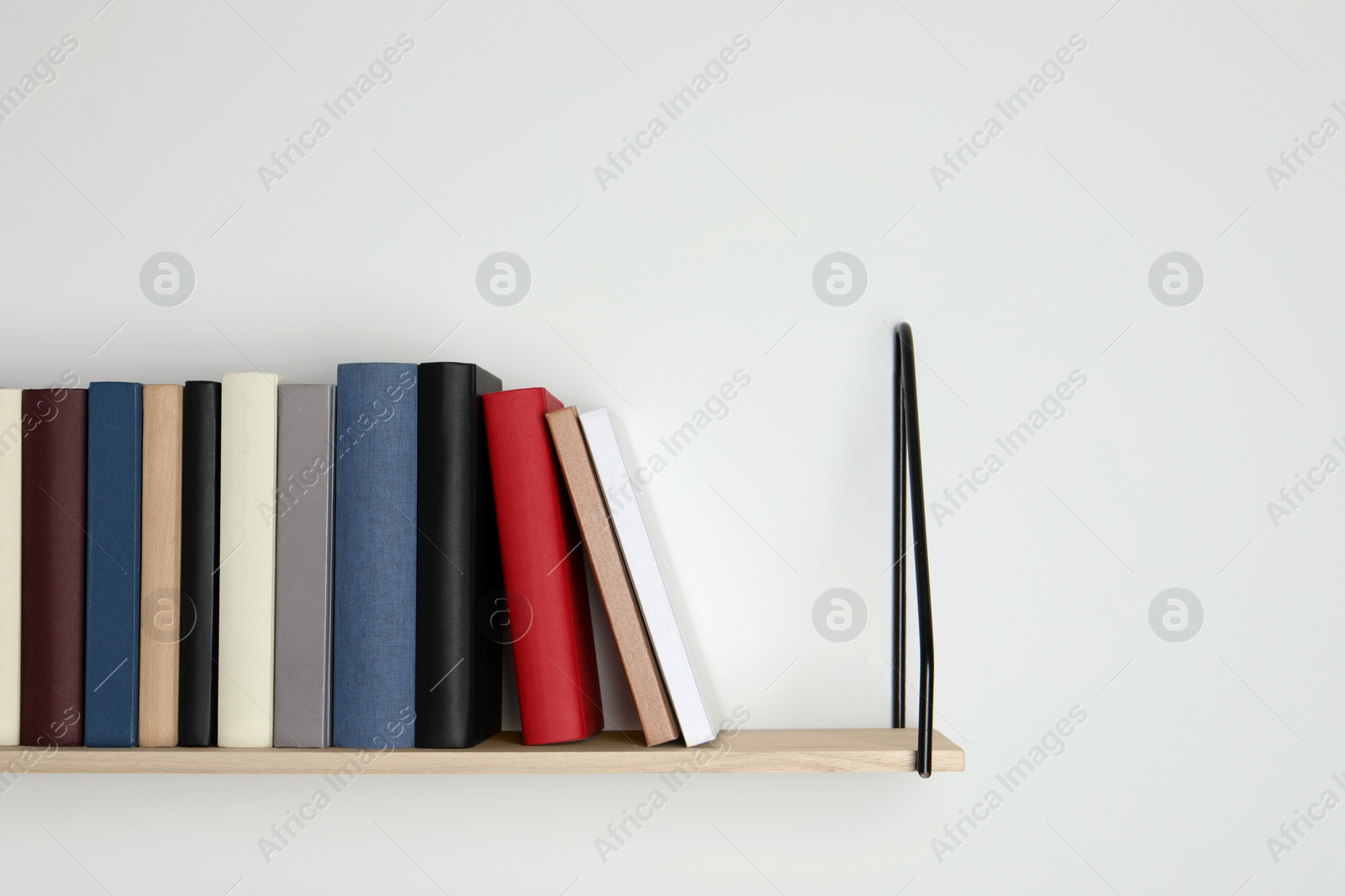 Photo of Wooden shelf with many hardcover books on white wall