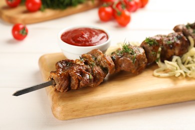 Metal skewer with delicious meat served on white wooden table, closeup