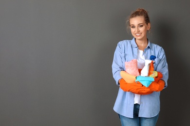 Woman with cleaning supplies on grey background