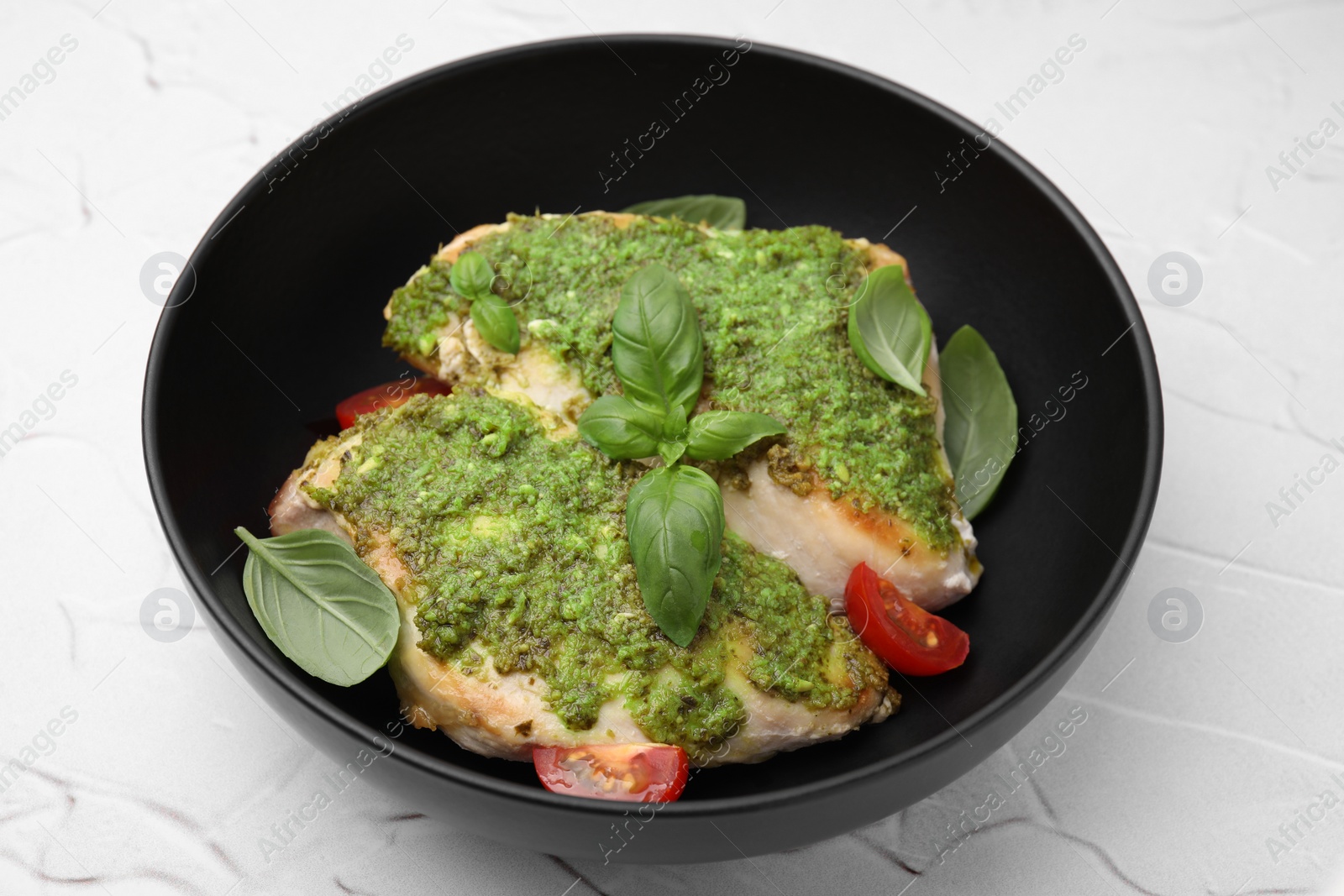 Photo of Delicious chicken breasts with pesto sauce, tomatoes and basil on white textured table, closeup