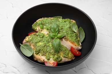 Delicious chicken breasts with pesto sauce, tomatoes and basil on white textured table, closeup