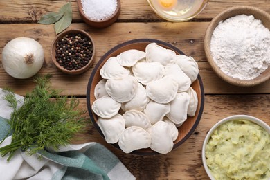 Raw dumplings (varenyky) and ingredients on wooden table, flat lay